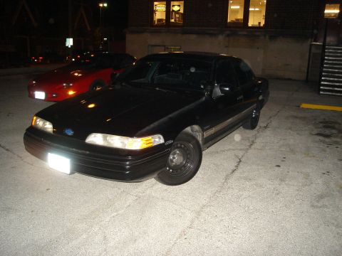 1992 Ford Crown Victoria - A black 1992 Ford Crown Victoria is parked outside a building at night, with another car visible in the background.