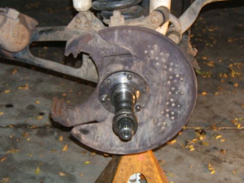 1988 Ford Bronco - Close-up of a vehicle's front wheel hub and brake rotor assembly, supported by a jack stand.