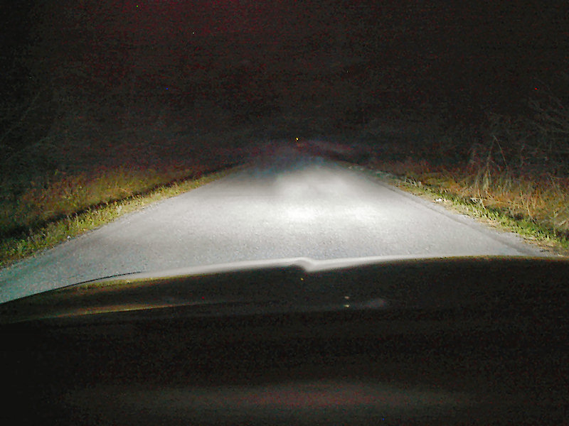 View from inside a car at night, headlights on a dark road. Supermotors.net logo visible