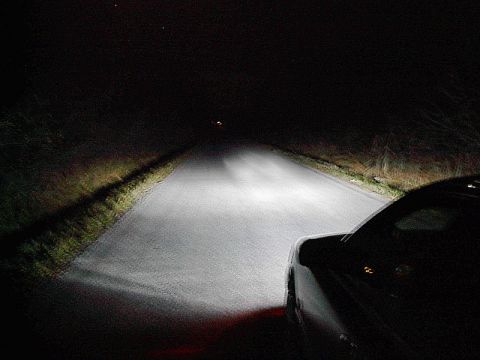 1985 Mercury Grand Marquis - Headlights illuminate a rural road at night, with the side of a car visible on the right.