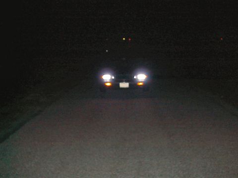 1985 Mercury Grand Marquis - Headlights of a car are visible at night on a road.
