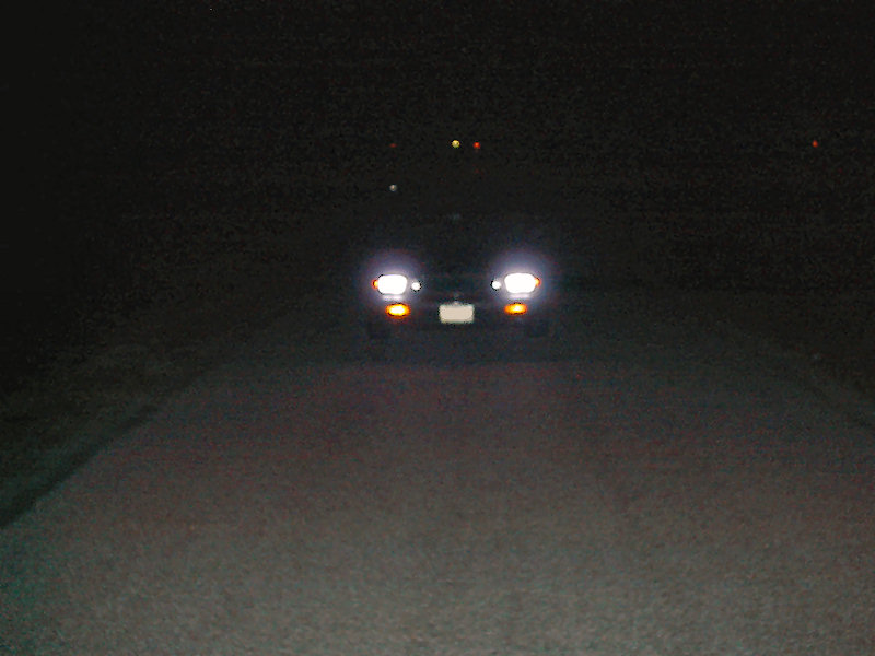 Car headlights and orange turn signals illuminate a dark road