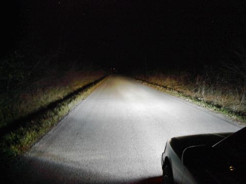 1985 Mercury Grand Marquis - A car's headlights cut through the darkness on a rural road, illuminating the path ahead.