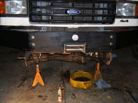 1988 Ford Bronco - Front axle and suspension of a 1988 Ford Bronco, lifted on jack stands for maintenance, a winch bumper and a Ford grille.