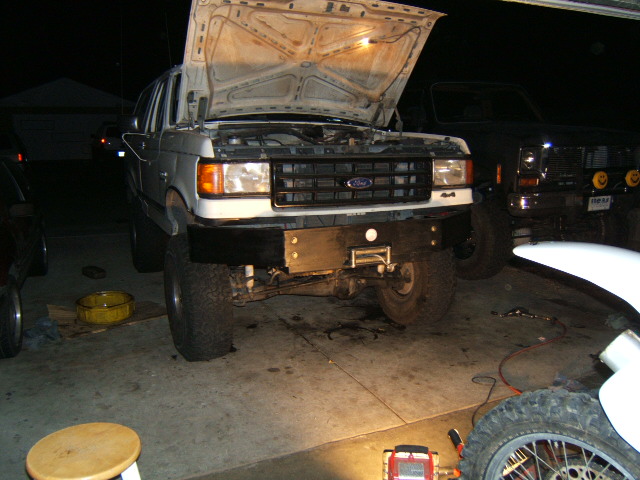 Lifted two-tone Ford 4x4 at night with hood up and winch bumper in driveway