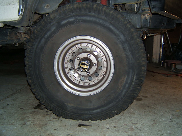 Mud-terrain tire on silver slotted wheel mounted on a truck in a garage