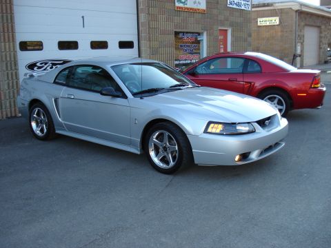 1998 Ford Taurus - Two Ford Mustangs, one silver and one red, are parked outside a garage.