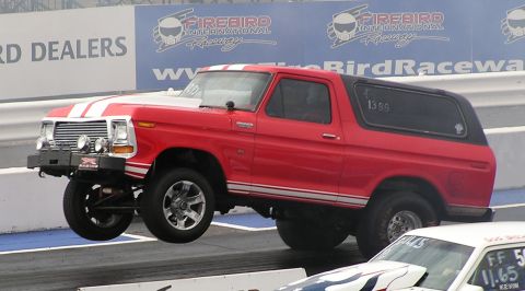 1979 Ford Bronco - A red 1979 Ford Bronco is airborne at a drag strip, with another vehicle visible in the foreground.
