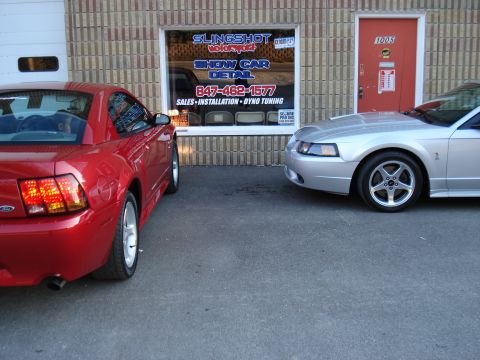 1998 Ford Taurus - Two Ford Mustangs, one red and one silver, are parked outside a car detail shop. The silver car appears to be from the early 2000s.
