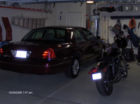 2004 Ford Crown Victoria - A maroon sedan is parked in a garage with a motorcycle beside it, showing the rear of the car.