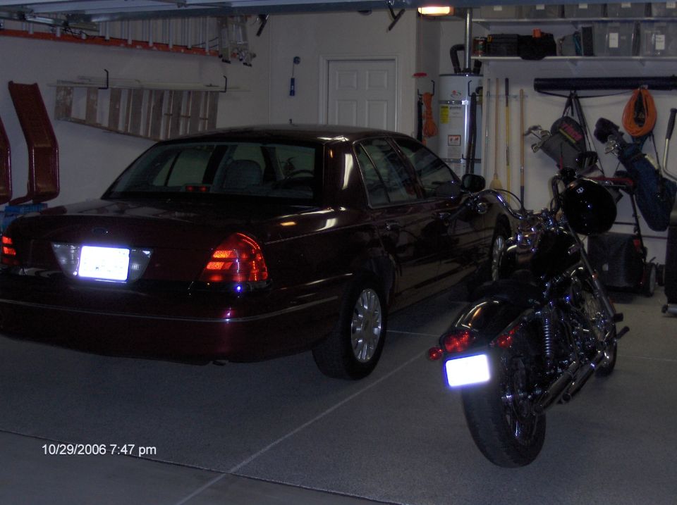 Maroon sedan parked in a garage next to a motorcycle. Rear view shows taillights and license plate