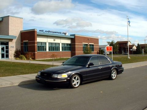 2000 Ford Crown Victoria - A dark blue 2000 Ford Crown Victoria is parked on the side of the road in front of a brick building.