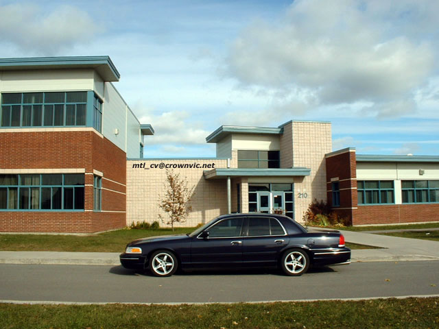 Dark blue Crown Victoria sedan, side view, silver wheels, parked by a brick building