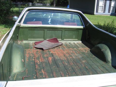 1973 Ford Ranchero - The bed of this Ford Ranchero shows significant wear and rust, with a small rug placed inside.