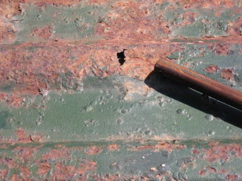 1973 Ford Ranchero - Close-up of heavily rusted corrugated metal with a shadow from a cylindrical object.