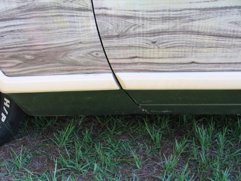 1973 Ford Ranchero - The distinctive woodgrain paneling on the side door of a 1973 Ford Ranchero is visible, along with a portion of the tire.