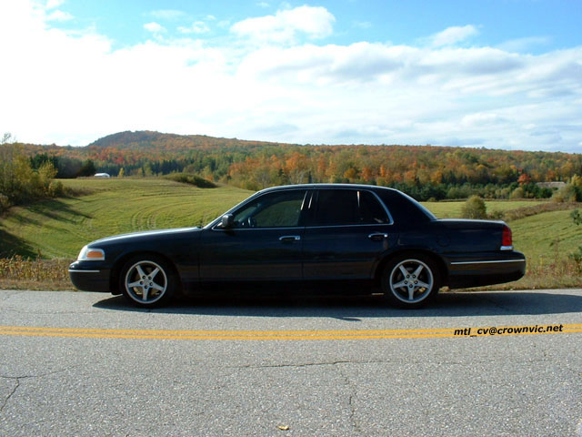 Dark gray Crown Victoria sedan in side profile on a road with fall-colored hills behind it