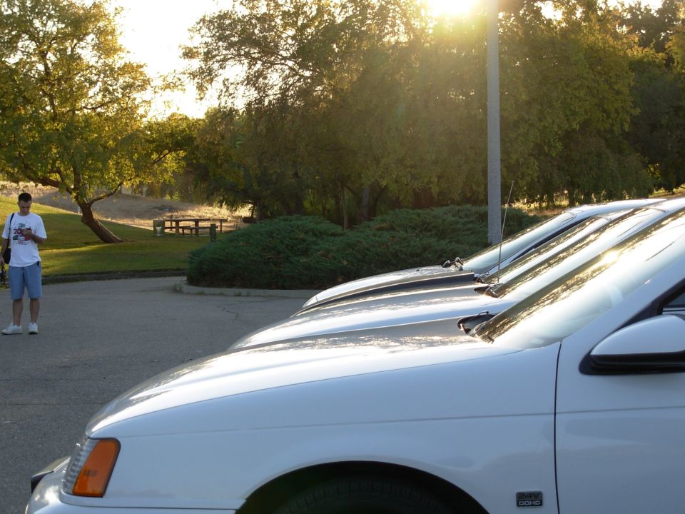 White sedan parked in a lot, front quarter view, with a person standing in the background