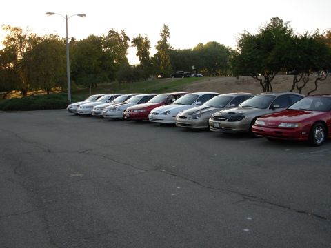 1995 Ford Taurus - A row of sedans, likely Ford Taurus models from the 1990s, are parked in a lot at sunset.