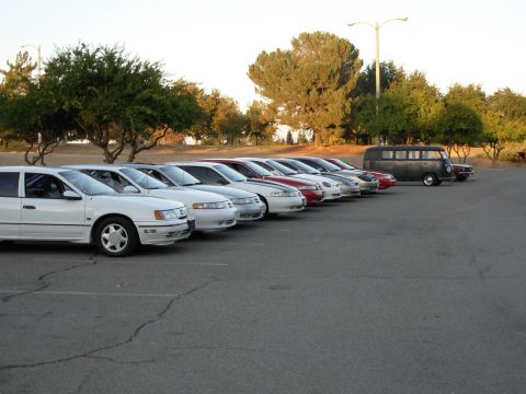 1995 Ford Taurus - Several sedans are parked in a lot, with a van and another car visible further back.