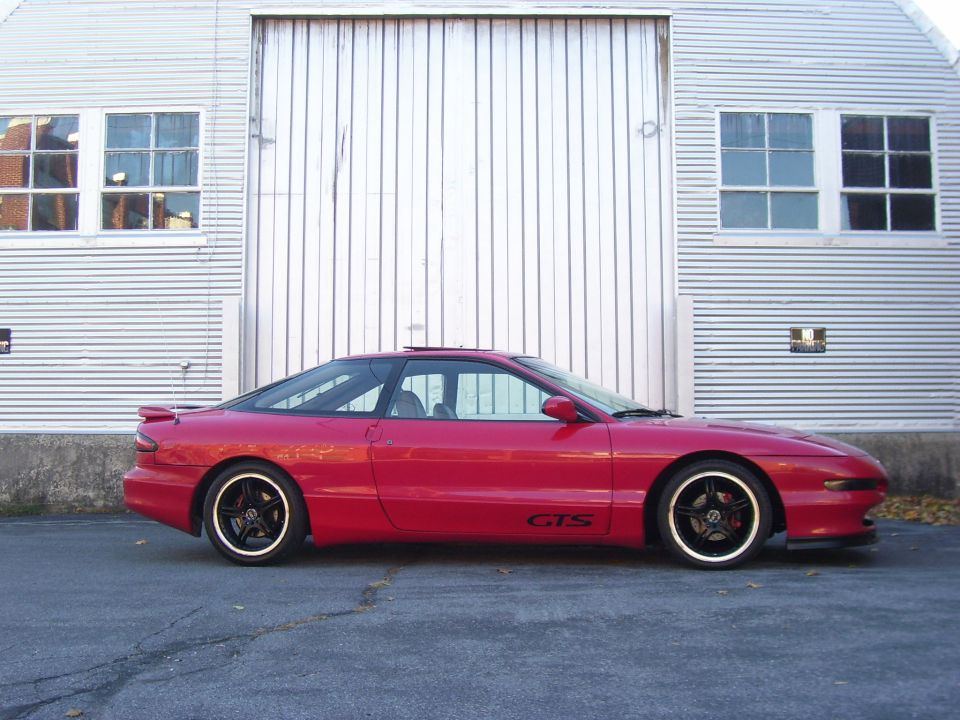 Red coupe with black roof and gold-trimmed wheels, side view