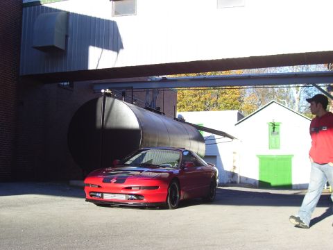 1997 Ford Probe - A red 1997 Ford Probe is parked in front of a large cylindrical tank and a white building.