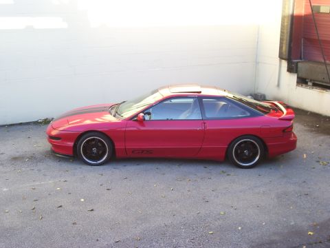 1997 Ford Probe - A red coupe with black racing stripes on the hood and a spoiler is parked outside.