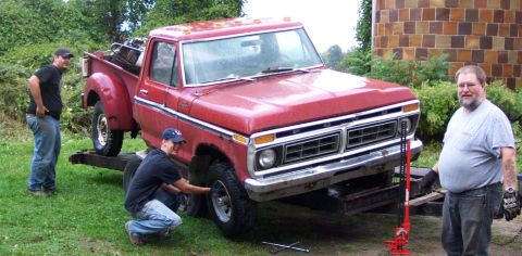 1975 Ford F-150 - Two men work on the front tire of a red 1975 Ford F-150 pickup truck being loaded onto a trailer.