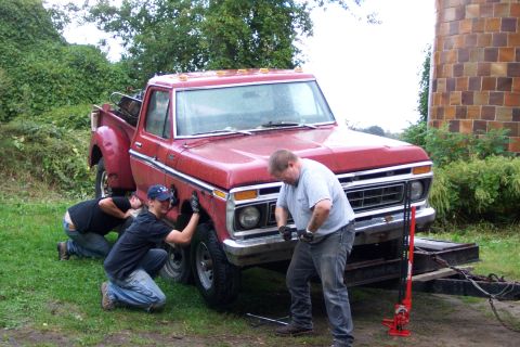 1975 Ford F-150 - Three men are working on the front fender and wheel of a red 1975 Ford F-150 pickup truck.