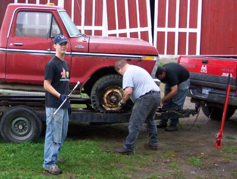 1975 Ford F-150 - A group of people work on the tire of a red 1975 Ford F-150 pickup truck.