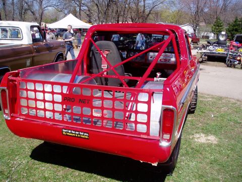 1986 Ford Bronco - A modified red pickup truck with a roll cage and racing seat is displayed at an outdoor event.