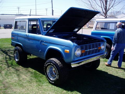 1986 Ford Bronco - A blue first-generation Ford Bronco is displayed with its hood open, alongside another similar vehicle.