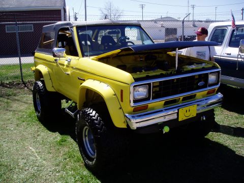 1986 Ford Bronco - A yellow Ford Bronco is parked on grass with its hood open, next to another vehicle.