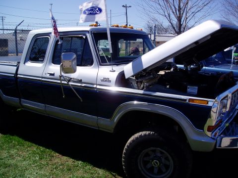 1986 Ford Bronco - This two-tone Ford pickup truck has its hood open and Ford flags flying from the roof.