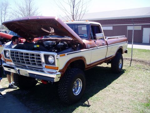 1986 Ford Bronco - A man looks at the engine of a lifted, two-tone Ford pickup truck parked on grass.