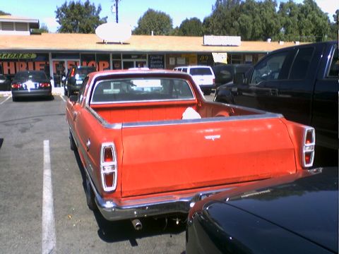 1973 Ford Ranchero - The rear of a red pickup truck is visible in a parking lot, parked next to other vehicles.