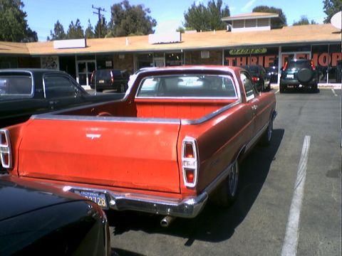 1973 Ford Ranchero - Rear view of a red pickup truck parked in a lot with a thrift store in the background.