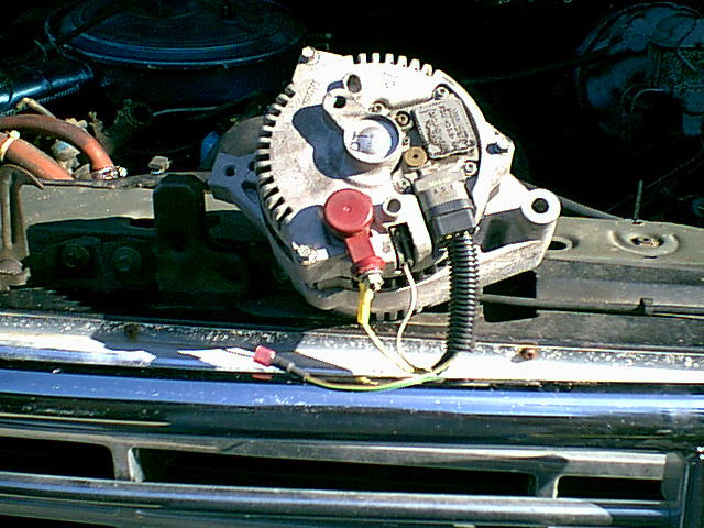 Alternator mounted in engine bay with red battery terminal and wiring
