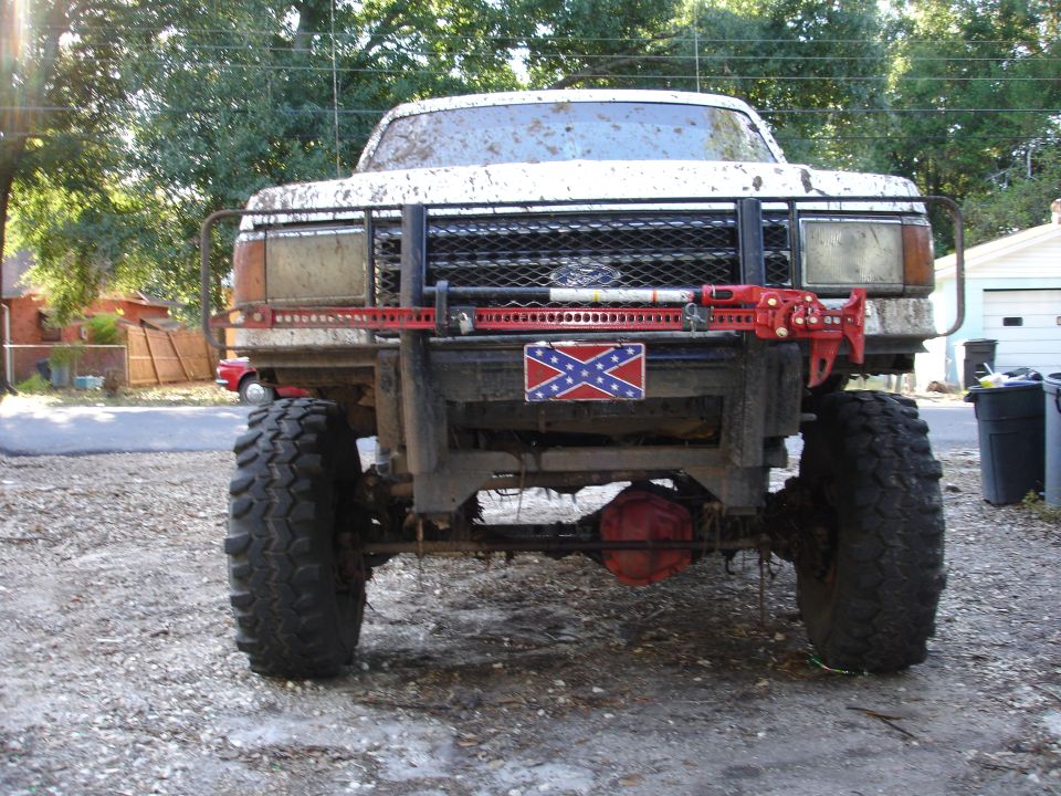 Mud-covered pickup truck with large tires, a winch, and a Confederate flag decal