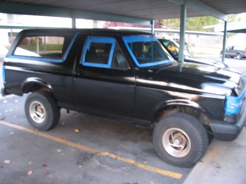1991 Ford Bronco - A black 1991 Ford Bronco is parked under a carport, with blue masking tape around the windows, suggesting it is being prepped for painting.