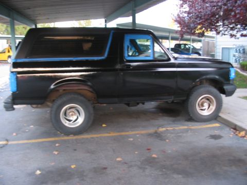 1991 Ford Bronco - A black 1991 Ford Bronco is parked outdoors, with blue painter's tape around the windows and rear bumper.