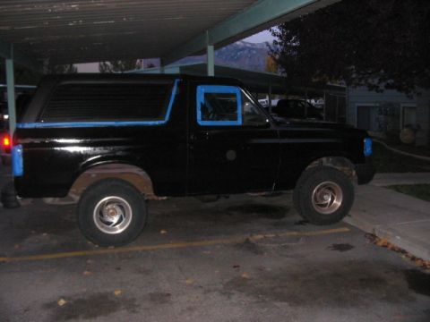 1991 Ford Bronco - Side view of a black SUV with blue masking tape on the windows and front fender.