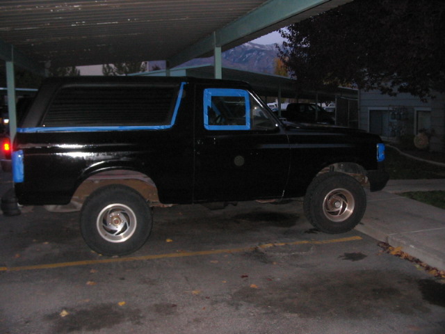 Black SUV with blue tape on windows and fender, parked under a carport