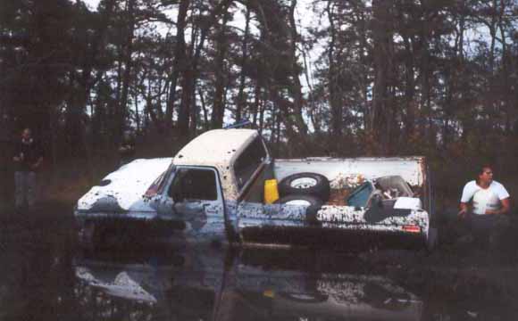 White pickup truck stuck in mud with spare tires in the bed