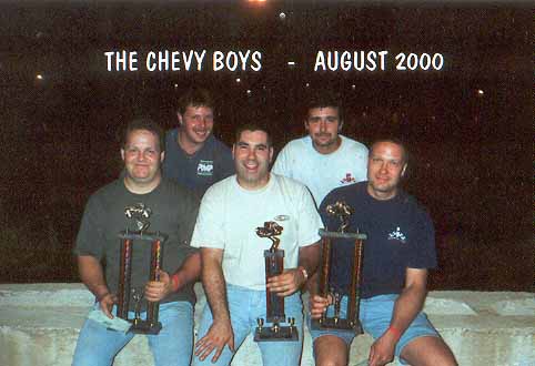 Five men pose for a photo holding trophies, with text 'THE CHEVY BOYS - AUGUST 2000' above them