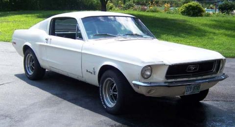 1968 Ford Mustang - A white 1967 Ford Mustang coupe is parked on a paved surface with a grassy area and trees in the background.