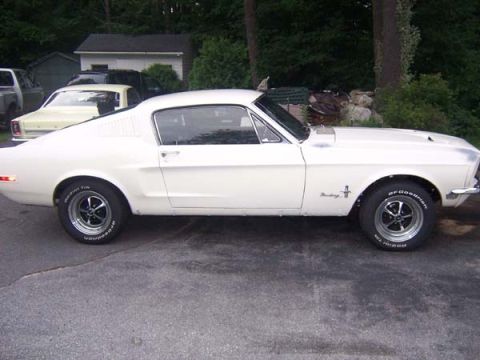 1968 Ford Mustang - A white 1968 Ford Mustang coupe is parked on asphalt with trees and buildings in the background.