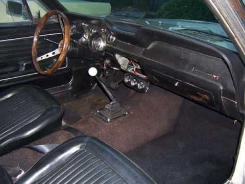1968 Ford Mustang - The interior of a 1968 Ford Mustang shows its dashboard, steering wheel, and shifter, with a 'Mustang' badge visible.