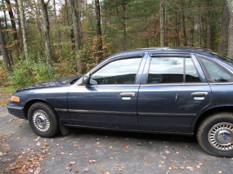 1991 Ford LTD Crown Victoria - A dark blue sedan is parked outdoors on a paved surface covered with autumn leaves.