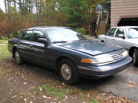 1991 Ford LTD Crown Victoria - A dark blue sedan sits in a driveway with another vehicle visible behind it.